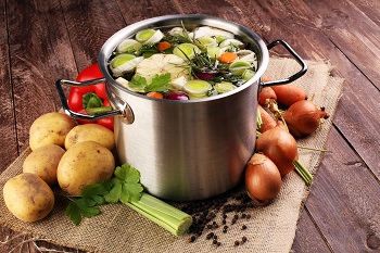 Ein großer Kochtopf, gefüllt mit frischen Zutaten in einer Brühe. Lauch, Kartoffeln, Zwiebeln und Kräuter.