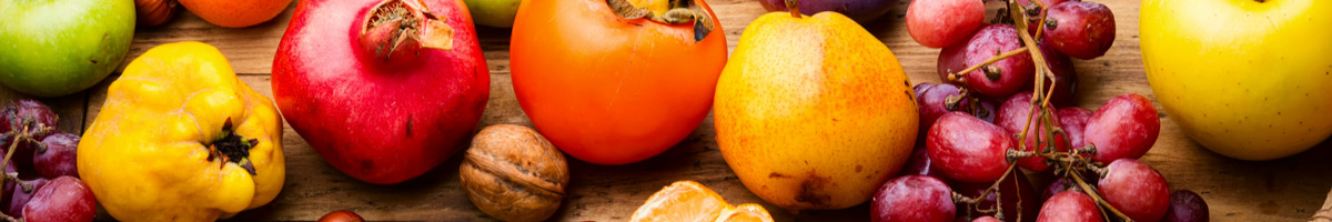 Gesunde Herbstfrüchte: Quitte, Apfel, Trauben, Walnüsse, Granatapfel, Mandarine und Birne, angerichtet auf einem Holztisch.